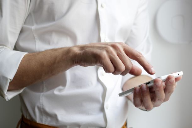 Nahaufnahme eines Mannes mit weißem Hemd tippt auf einem Handy