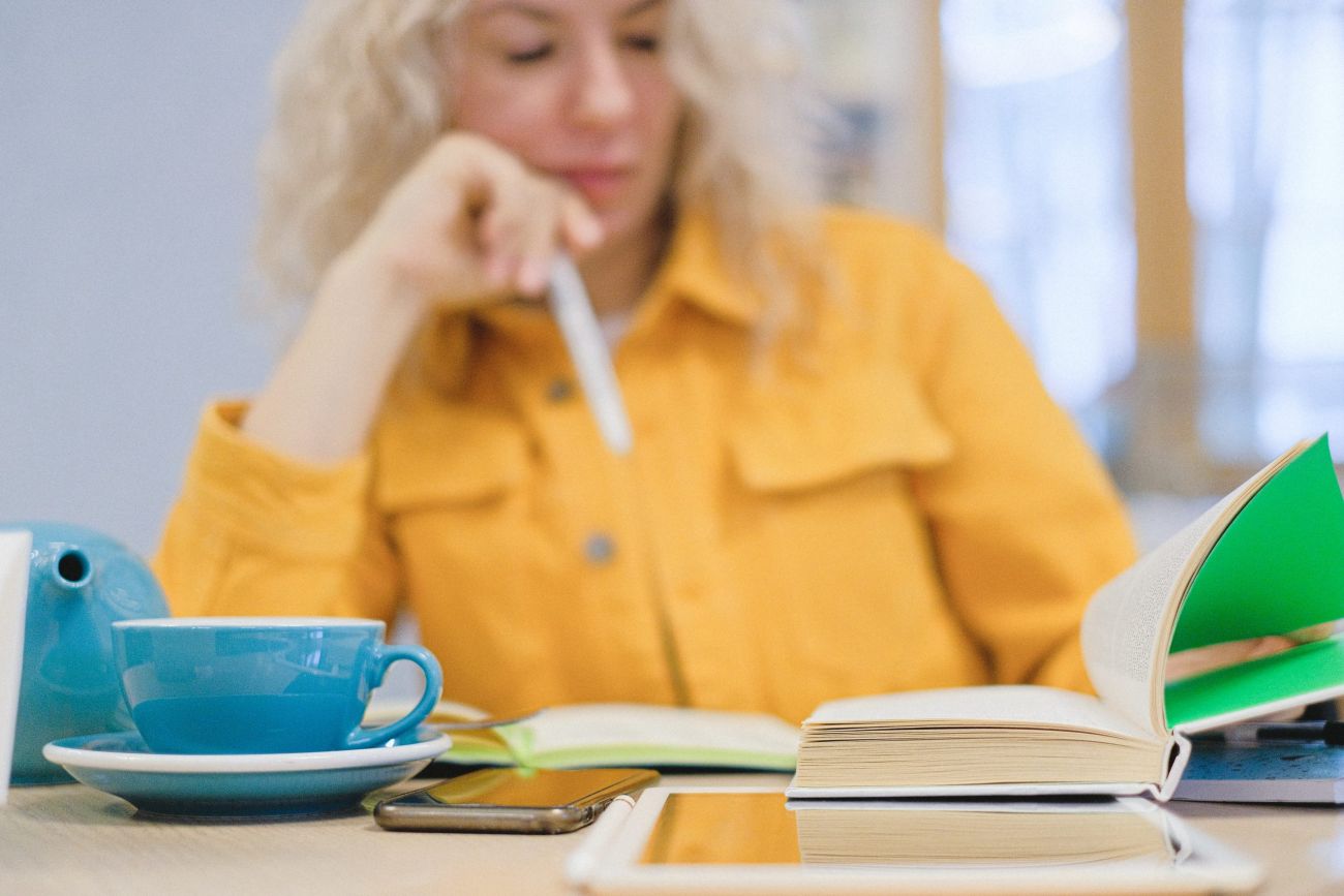 Frau in gelbem Hemd,unscharf zu sehen. Ein Tisch mit einer Teetasse, einem Handy und einem Buch.
