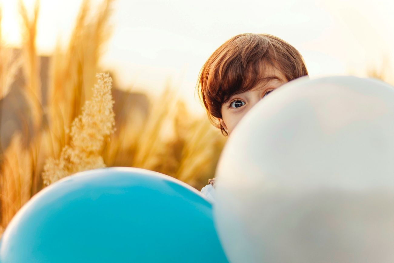 Zwei Luftballons in einem Kornfeld, ein Kindergesicht ist halb sichbar.
