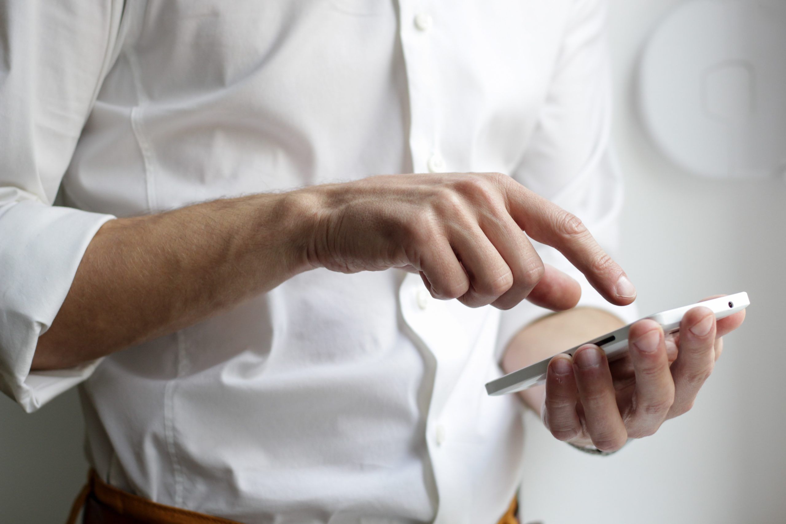 Nahaufnahme männliche Person mit weißem Hemd tippt auf einem Handy