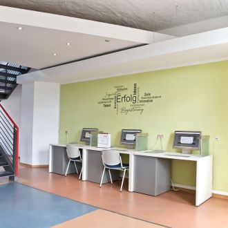 Drei zusammengestellt Schreibtische mit Monitoren, Tastaturen und Mäusen an einer Wand.