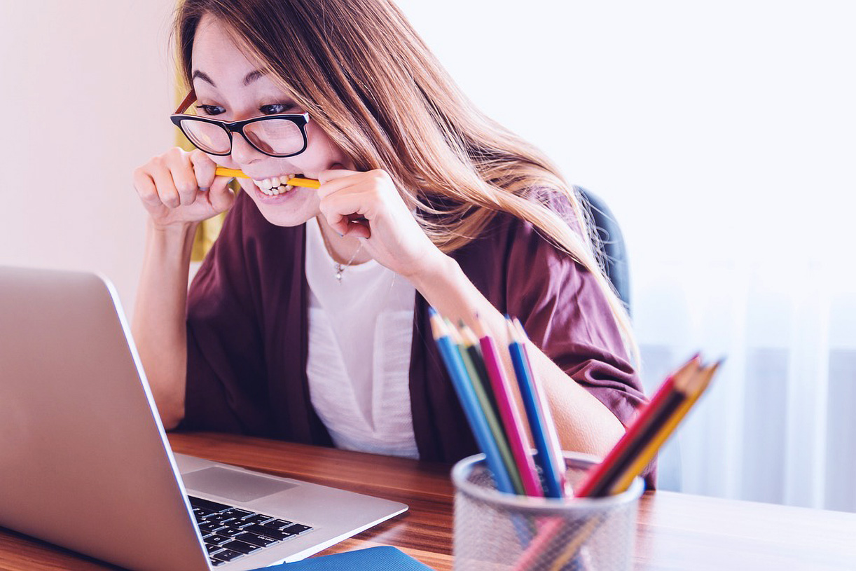Junge Frau beißt auf einen Bleistift, während sie auf einen Laptop schaut.