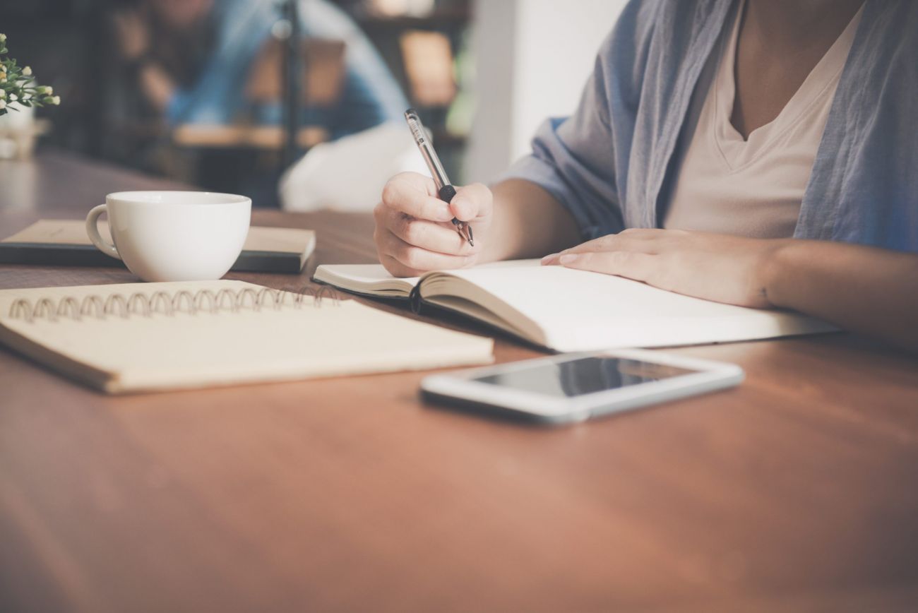 Holztisch mit Notizheften und eine Person mit Stift in der Hand.