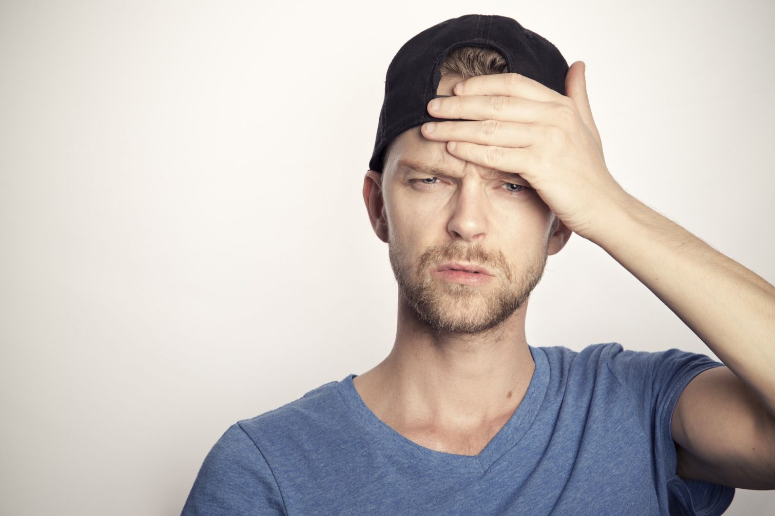 Ein junger Mann fasst sich stirnrunzelnd an den Kopf, er hat ein Basecap auf